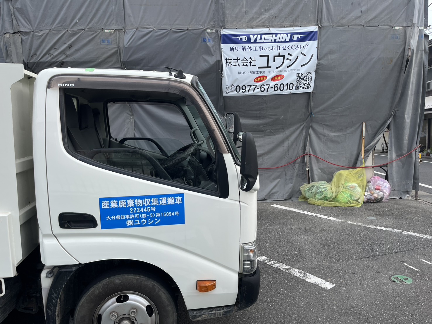 亀川の解体工事現場に設置された株式会社ユウシンの横断幕と作業車